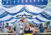 Oktoberfest Celebrations In and Around Pittsburgh 2025 A man and woman stands in front of an Oktoberfest Pittsburgh sign outside.
