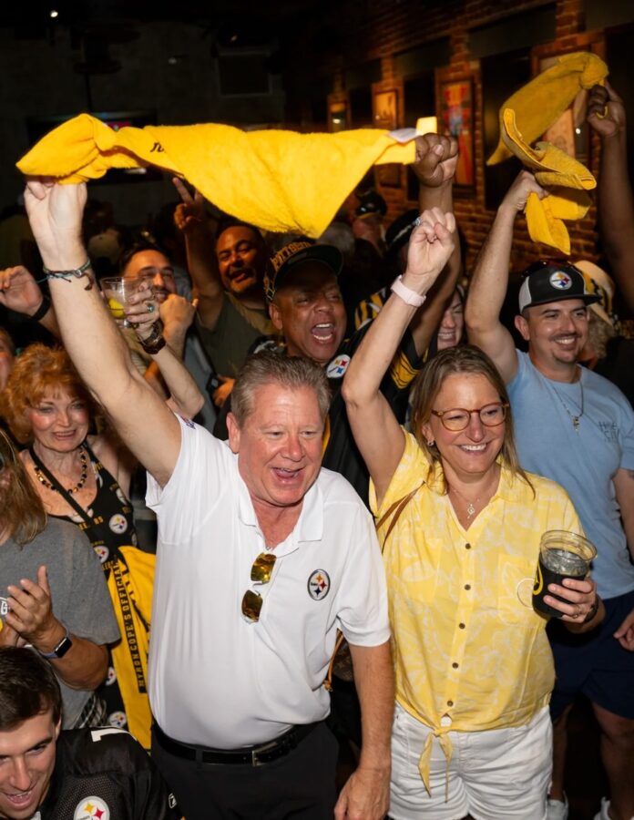 A group of Pittsburgh Steelers fans cheer and wave terrible towels watching the game in a sports bar.