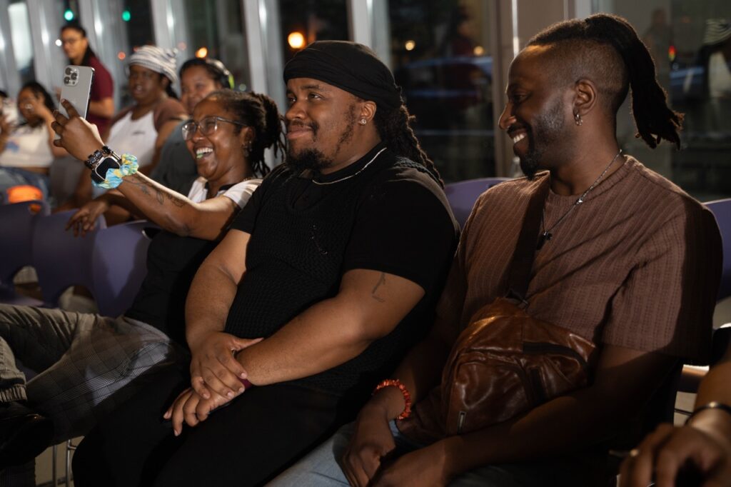 A group of people sit in purple shows, watching a performance at Pride and Joy at the August Wilson Center.