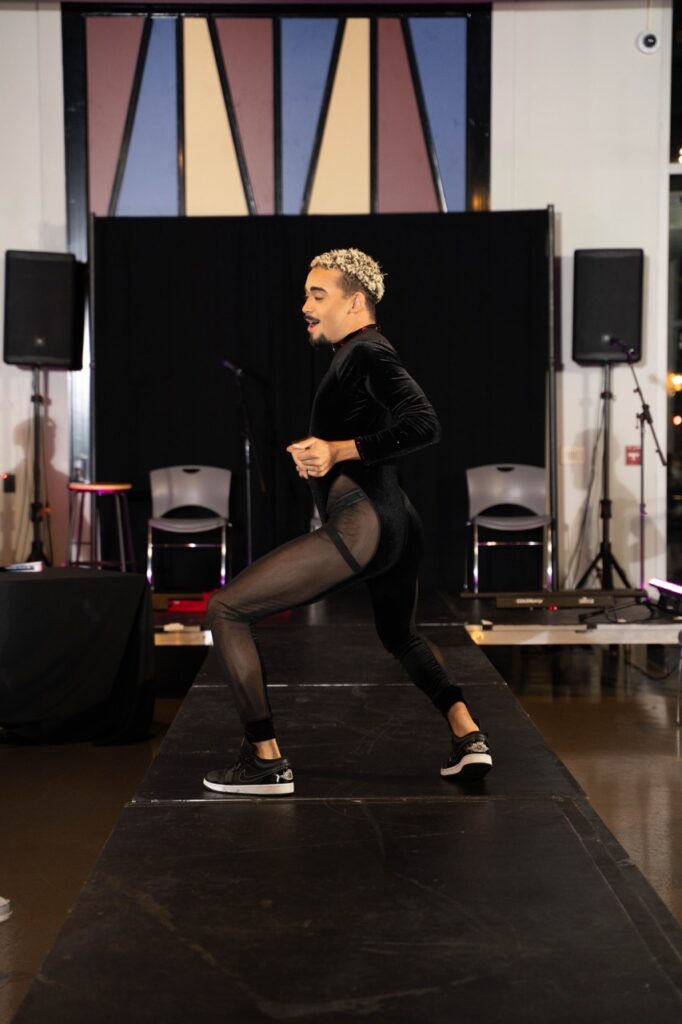 A person in a tight black leotard dances on a catwalk.