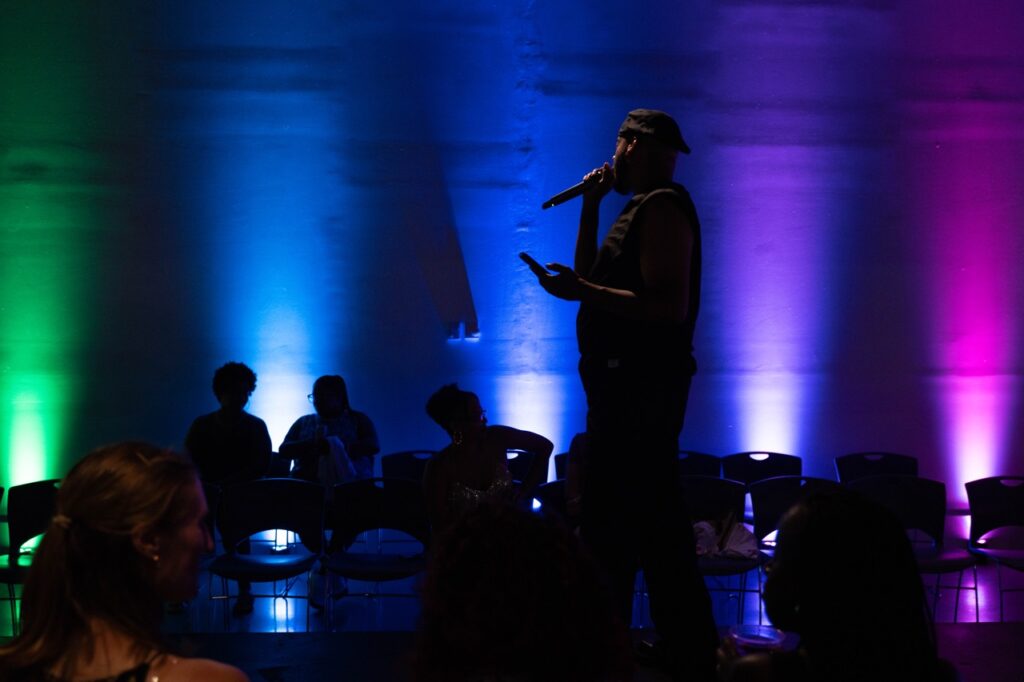 A man signs into a mic in front of colored lights.
