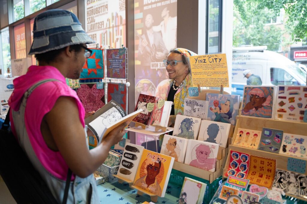A person looks through a book at a queer market vendor table.