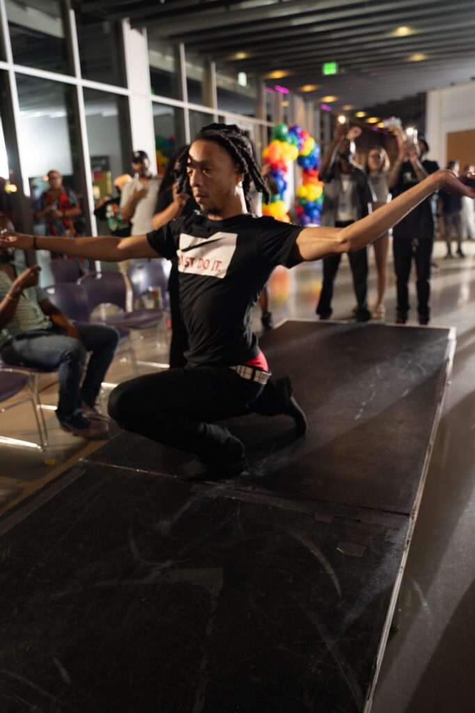 A man drops down while dancing on a black catwalk.