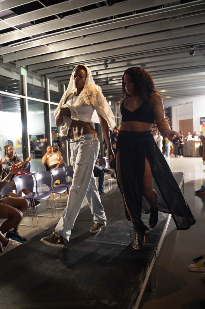 A woman in black and a woman in white walk down the catwalk together.