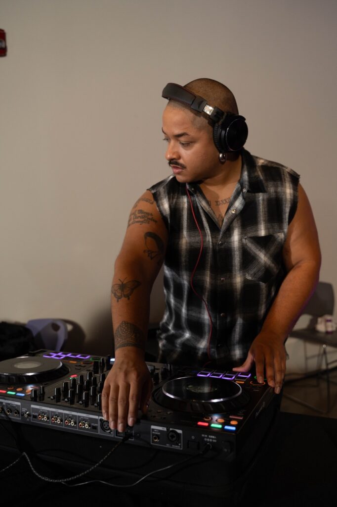 A person in a black and white cut off flannel DJs music with headphones on.
