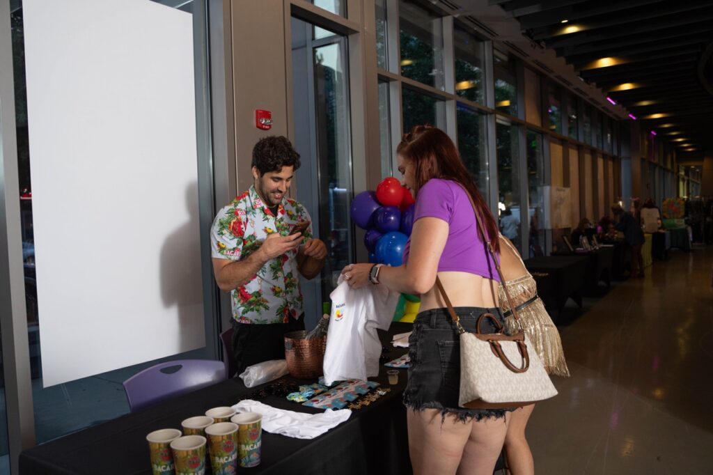 A woman in a purple shirt picks up a shirt from a Pride and Joy vendor.