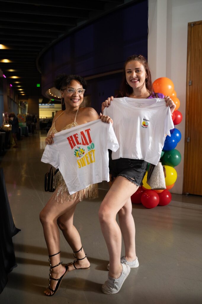 Two women hold up white shirts with their knee popped out.