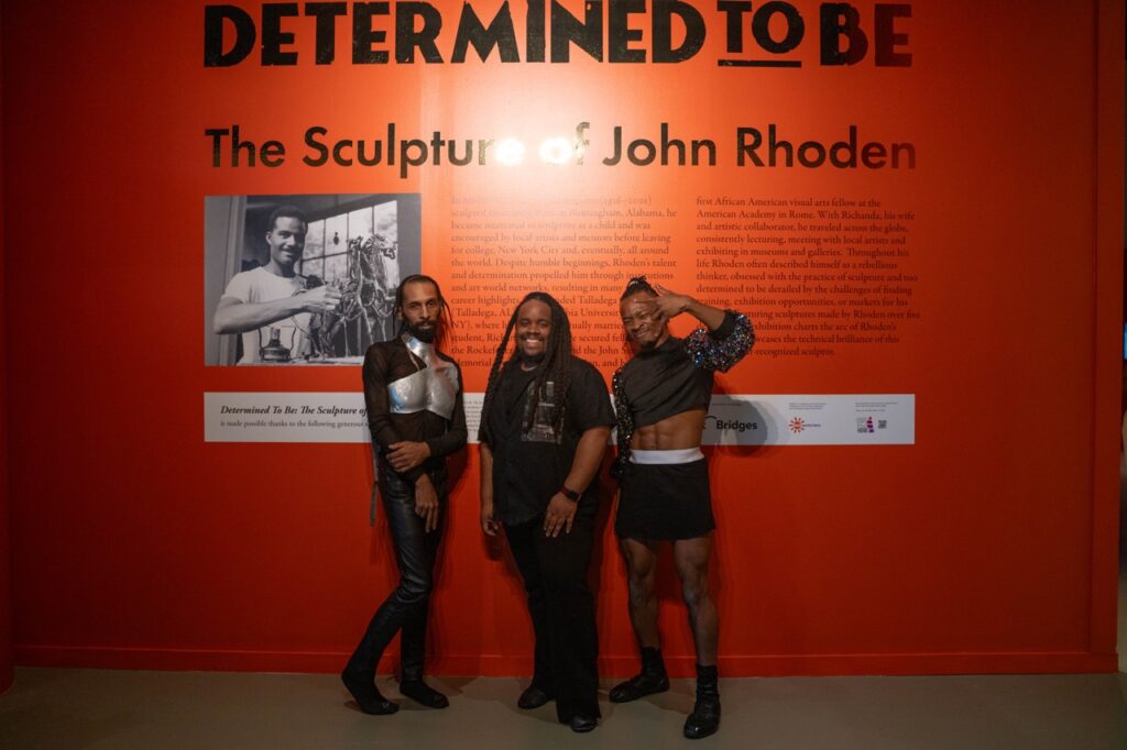 Three men stand in front of a red wall exhibit at the August Wilson center in Pittsburgh.