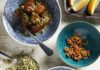 Roasted Eggplant with Anchovy and Almond Crumble Blue-and-white patterned bowls filled with roasted eggplant, topped with a green crumble, with a separate bowl of dried anchovies.