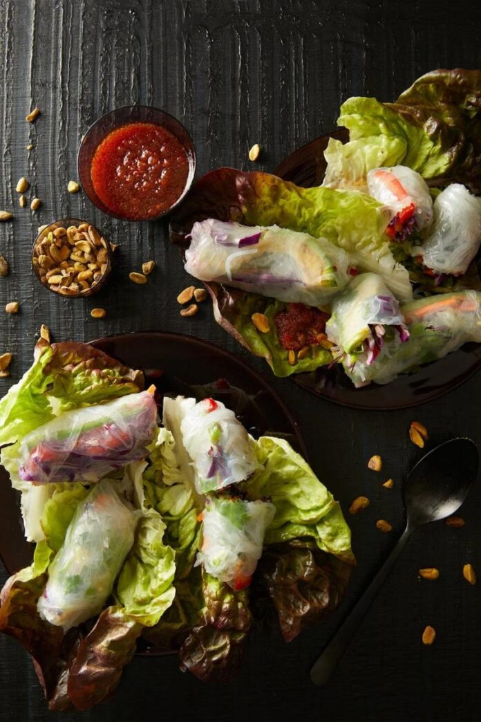 A flat lay of fresh spring rolls with a sweet potato noodle filling, arranged on lettuce leaves with a side of dipping sauce and roasted peanuts.