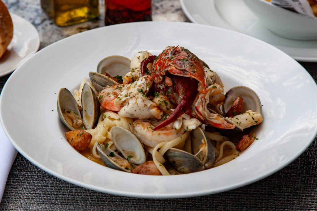 A white pasta bowl with a seafood pasta including lobster, shrimp, and clams.

