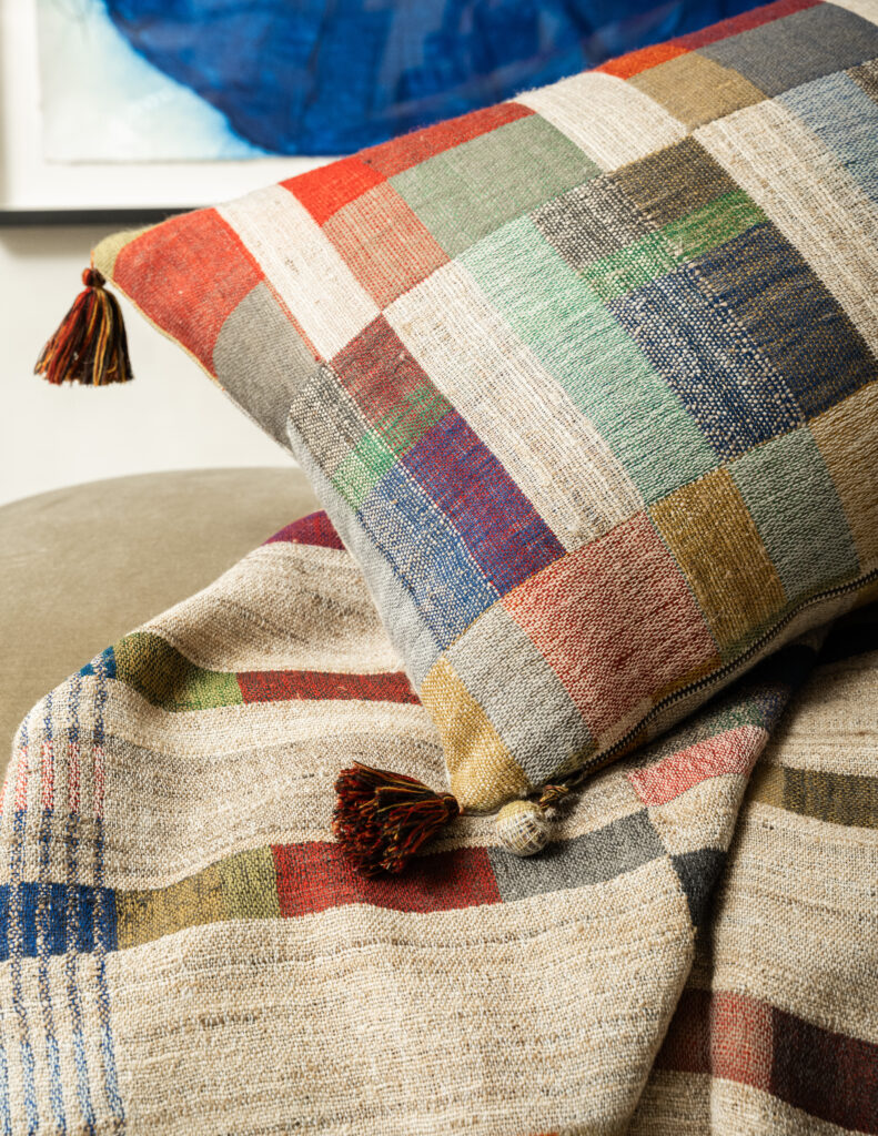 A pillow with various jewel town squares and rectangles sits on a blanket of the same pattern.