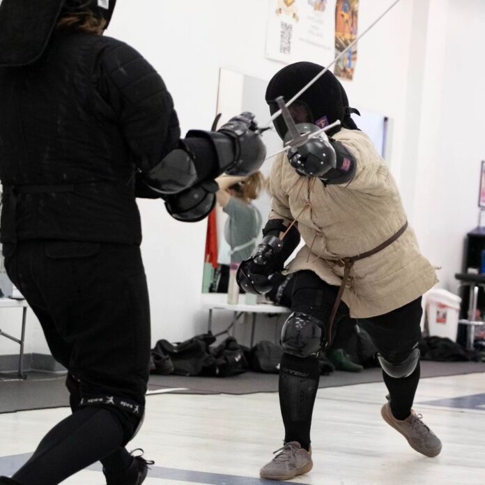 Two adults fencing in a class in the fall.