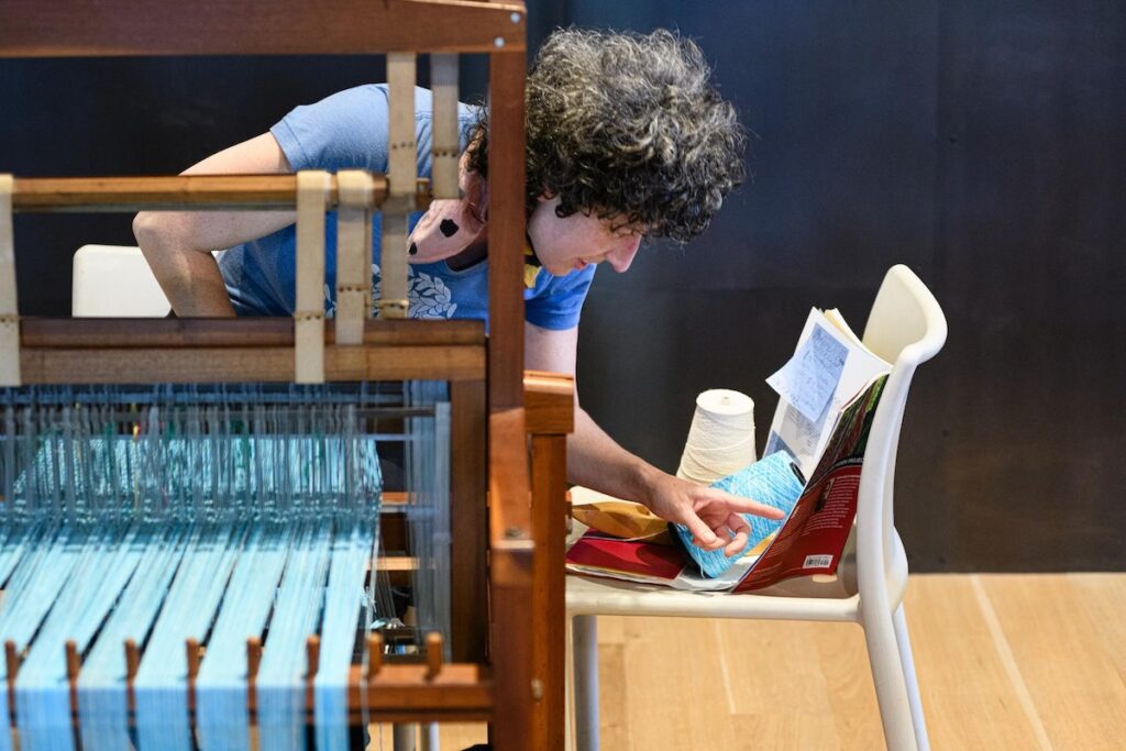 A staff member at Contemporary Craft stands over a loom. 