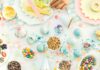 Apple Donuts, A Healthy Kids Treat A colorful overhead view of a table with plates of sliced apples decorated to look like donuts with various toppings, with bowls of candy and sprinkles, and children's hands reaching for the food.