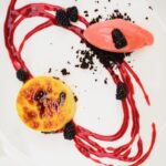 A white plate holds a blackberry creme brulee with a blackberry swirl around the plate and a small scoop of ice cream.