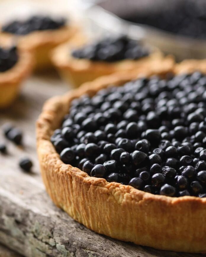Blueberry Concord Grape Tart TABLE Magazine A large, rustic tart with a golden crust filled to the brim with fresh blueberries.