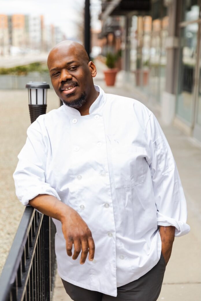 Café Momentum’s Chef Shares His Favorite Pittsburgh Breakfast Spots Chef Robert Carter at Pittsburgh breakfast spot Cafe Momentum leans against a railing in a white chef's coat.