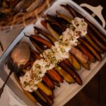 A white tray full of Carrot Casserole with a white sauce and pistachios on top.