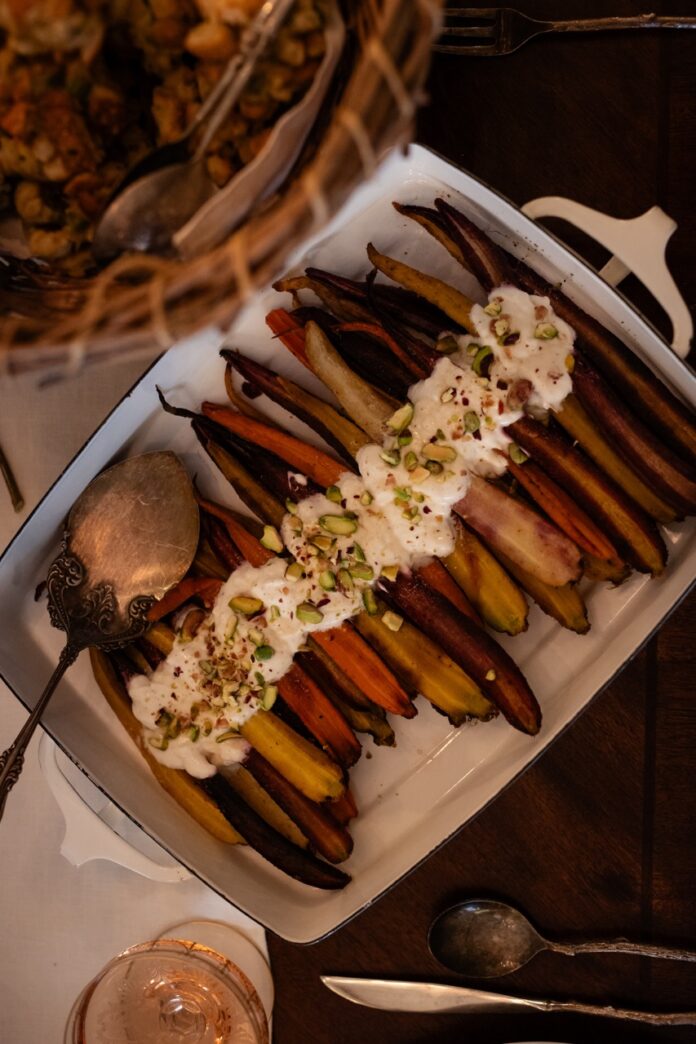 Carrot Casserole A white tray full of Carrot Casserole with a white sauce and pistachios on top.
