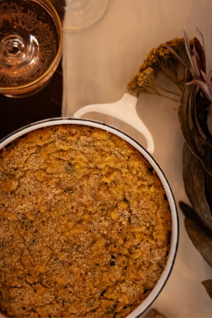 Corn Casserole A round skillet in the corner of corn casserole beneath a drinking glass.