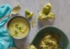 Farm Fresh Fall Recipes A bowl of zucchini noodles on a blue plate, with a fork holding some noodles above the bowl, alongside a bowl of zucchini soup and other ingredients on a gray table.