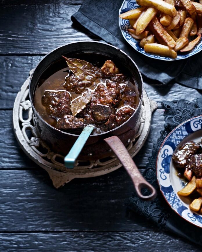Dutch Treat TABLE Magazine A large, copper pot of beef stew with bay leaves, a small plate of the stew next to a larger plate of french fries.