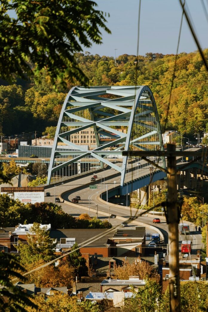 Top Spots for Viewing Fall Foliage in Pittsburgh Colorful trees turning in the fall season to a yellow color around a bridge in Pittsburgh.