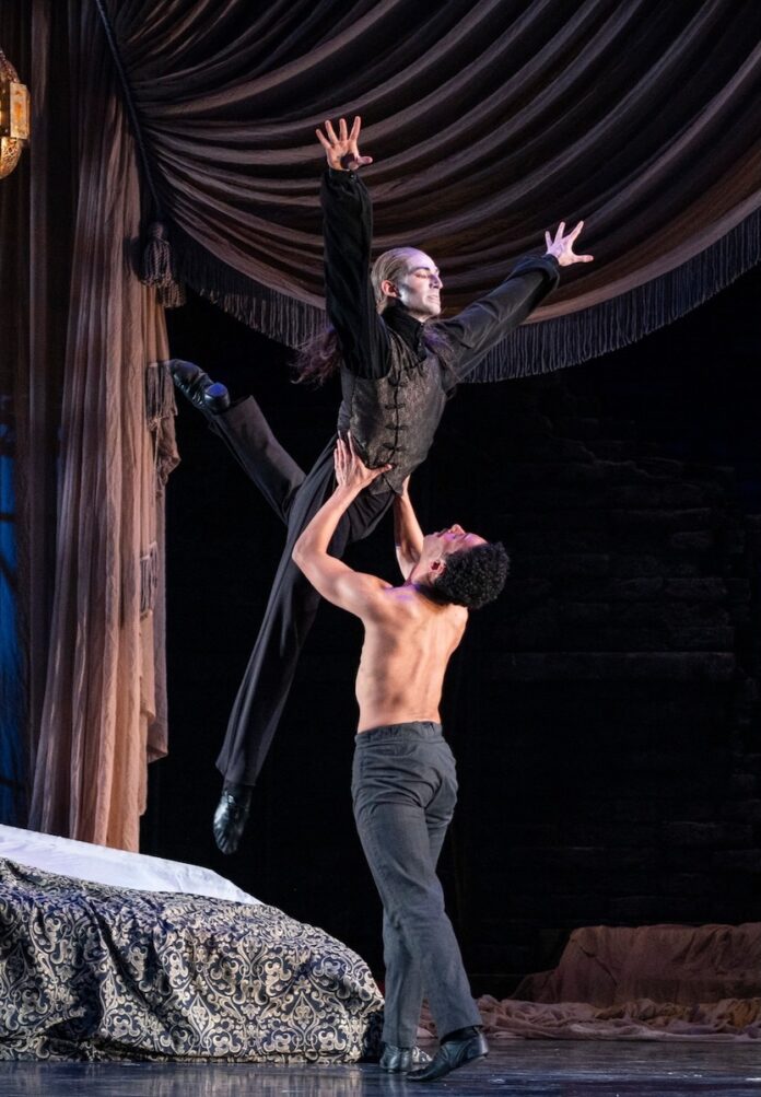 A shirtless dancers lifts a Dracula dancer in a Halloween dance performance.