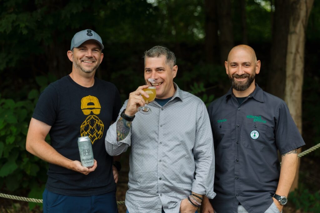 Three men from Hyeholde and Altered genius Brewing Co. stand together holding beer.