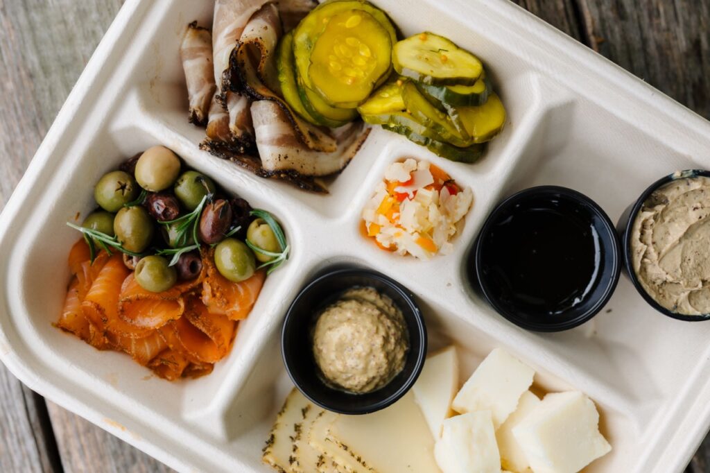 A charcuterie board to-go with meats, cheese, pickles, and more.