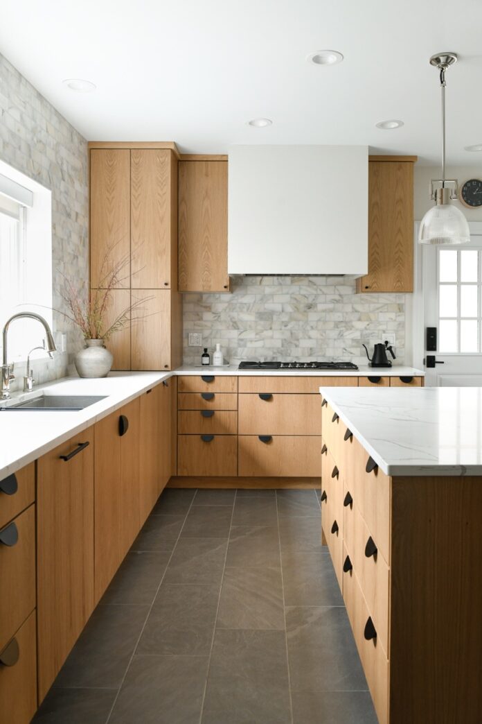 An interior of a kitchen with pale wood cabinets, white countertops and walls, and black embellishments all designed by Katy Popple.