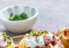 Using Leftover Chili in New Recipes A platter of three loaded baked potatoes topped with recipes like leftover chili, sour cream, bacon bits, and chopped chives.