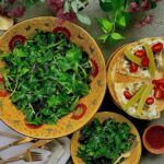 A large bowl of fresh, leafy green salad with a smaller serving on a plate with pita bread