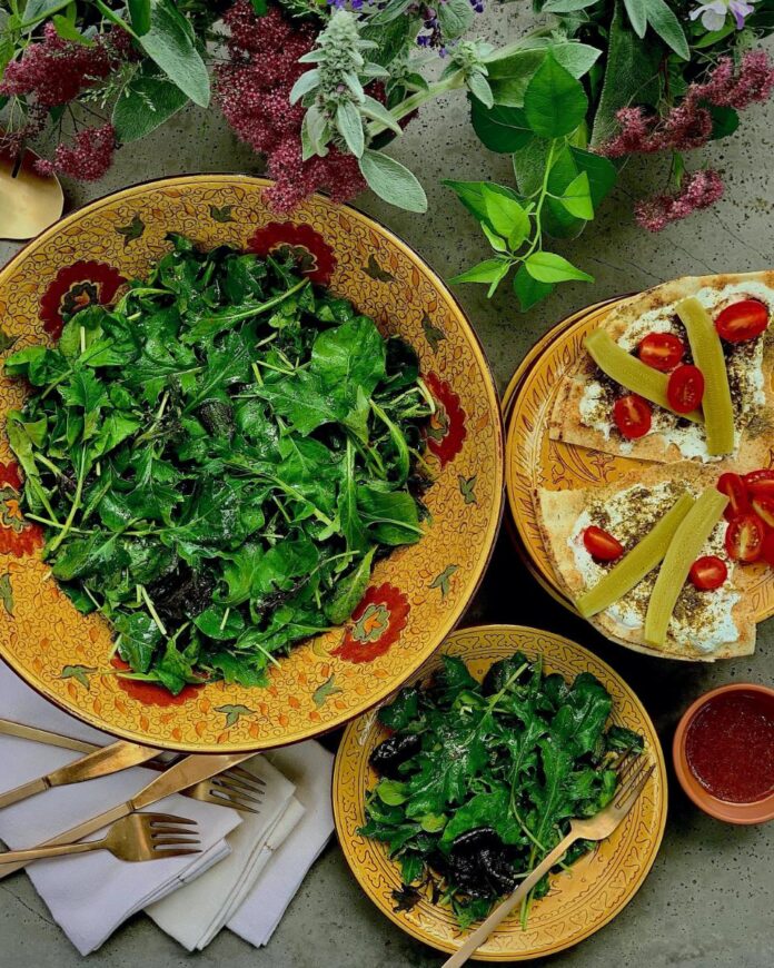 Maple Curry Salad Dressing TABLE Magazine A large bowl of fresh, leafy green salad with a smaller serving on a plate with pita bread