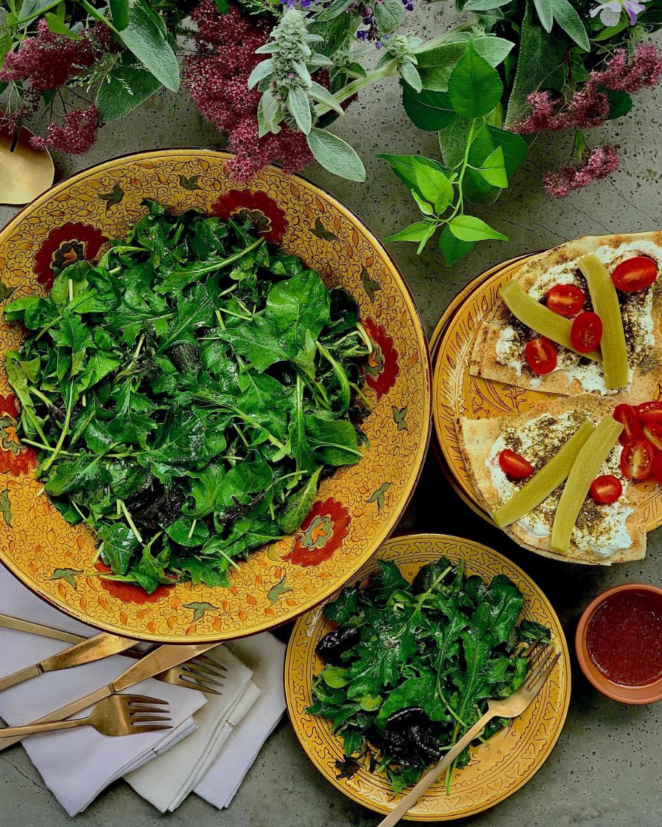 A large bowl of fresh, leafy green salad with a smaller serving on a plate with pita bread