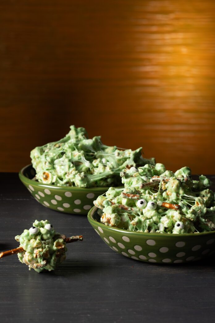 Two green polka-dot bowls filled with Marshmallow Monster Popcorn, with pretzel sticks and candy eyes.