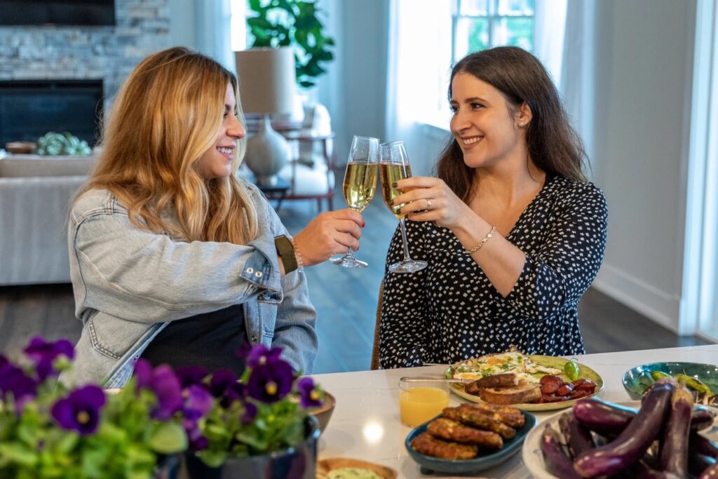 Two women cheers champagne flutes at a counter.