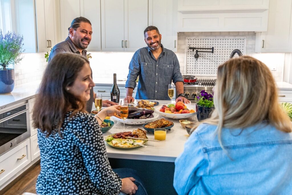 A group of people talk around a breakfast feast at a counter.