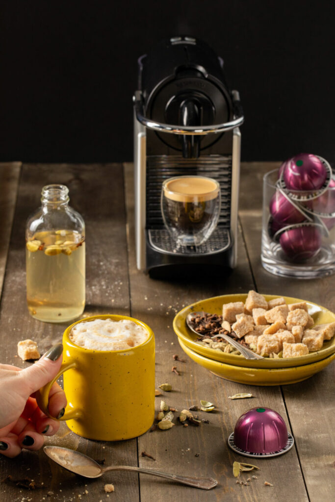 A cardamom and clove oat milk latte in front of a small espresso machine.
