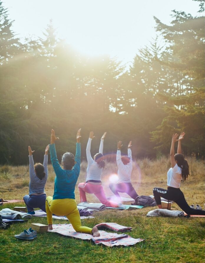 A group of people do yoga outdoors in the woods.