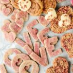 Heart-shaped and round cookies, some with a pink sugar dusting, arranged on a marble surface to spell out the word "LOVE" with individual letters.