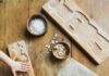 Speculaas Gingerbread Cookies Two wooden gingerbread cookie molds, one of which a child's hands are pressing dough into, next to a ball of dough, a rolling pin, and small bowls of flour and sliced almonds.