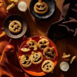 Red platter of jack-o-lantern shaped apple raisin hand pies, with two pies on separate black plates.