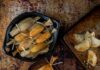 Tamales and Tradition A black bowl filled with traditional tamales wrapped in corn husks, with one unwrapped tamale on a smaller plate showing a rich, red filling. Beside the plates are other New Mexican foods, including empanadas and biscochitos.