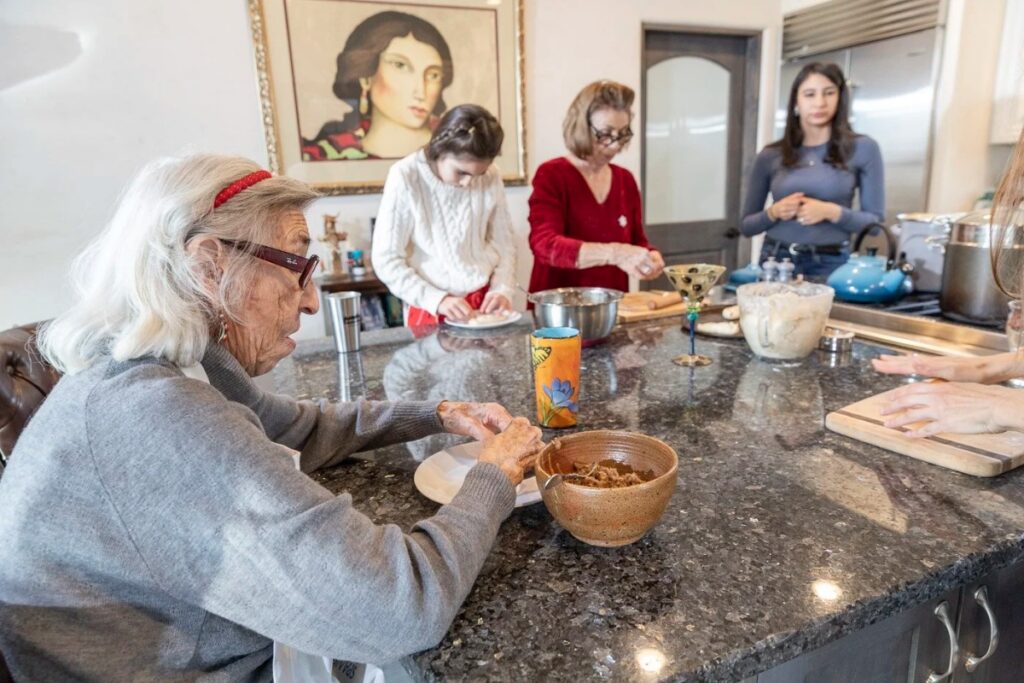 Four generations of women from the Martinez family, gathered in a kitchen around a large island, making cookies and tamales.