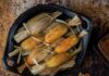 Traditional Tamales A black bowl filled with traditional tamales wrapped in corn husks, with one unwrapped tamale on a smaller plate showing a rich, red filling.