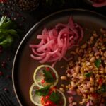 A plate with a farro and black-eyed pea salad, topped with pickled red onions and garnished with lemon slices, parsley, and red chilies.