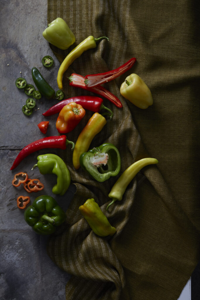 Green, orange, yellow, and red peppers lay on a table. 