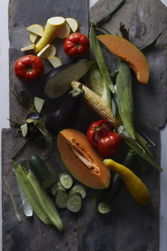Vegetables lay about from local farms on a black sheet of paper.